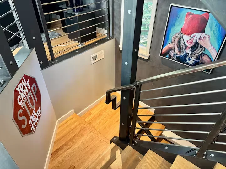 Multi-level timber staircase with steel-and-cable railings, framed portrait artwork and a decorative stop sign