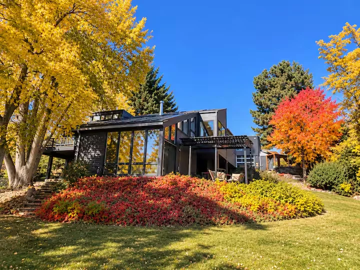 Dark contemporary residence viewed from the backyard lawn, surrounded by yellow trees and red autumn foliage