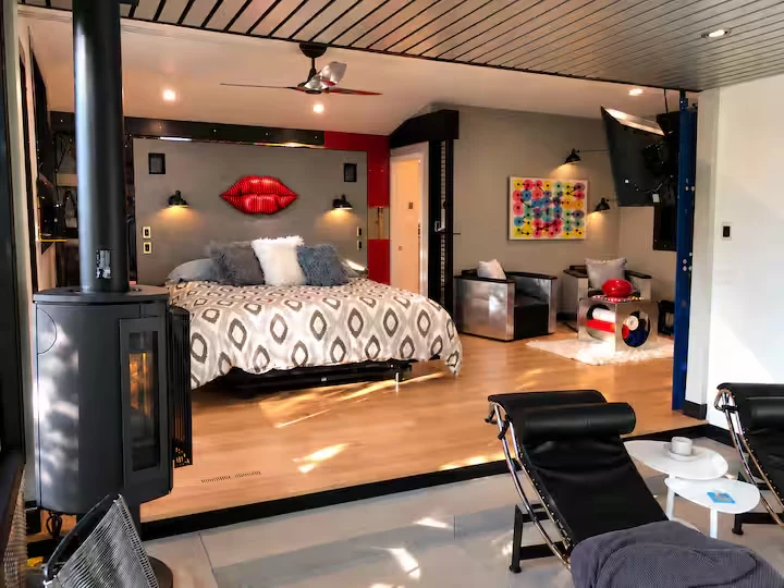 Primary suite viewed from the lounge, with bed, red lips artwork, metal chairs and hardwood floor