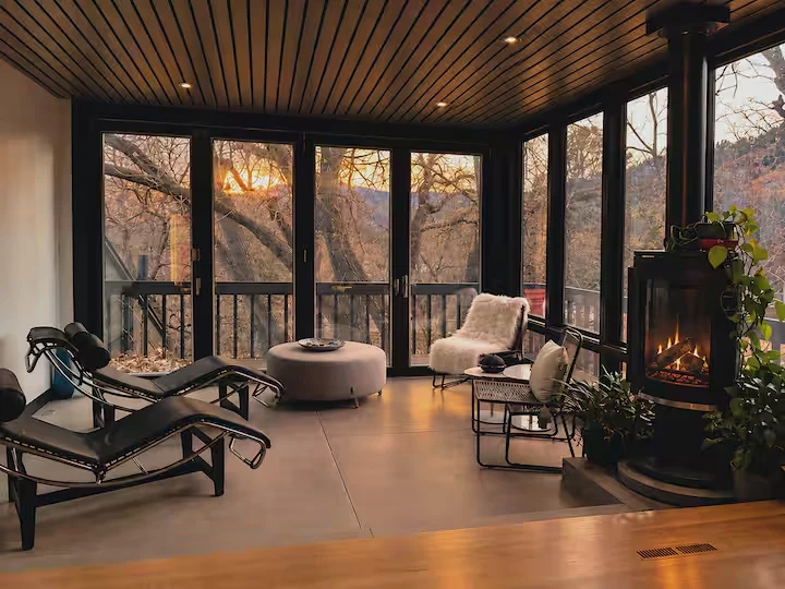 Private sitting lounge at dusk with recliners, fireplace and treetop views through glass doors