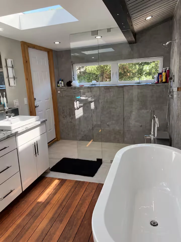 Primary bathroom with freestanding white tub, glass shower, vanity and skylight