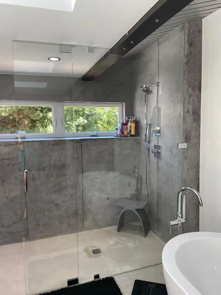 Curbless glass shower with concrete walls, overhead fixture and garden-facing window