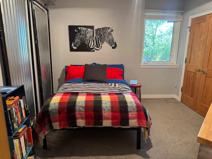 Third guest bedroom with plaid blanket, red and blue pillows, zebra artwork and a tree-facing window