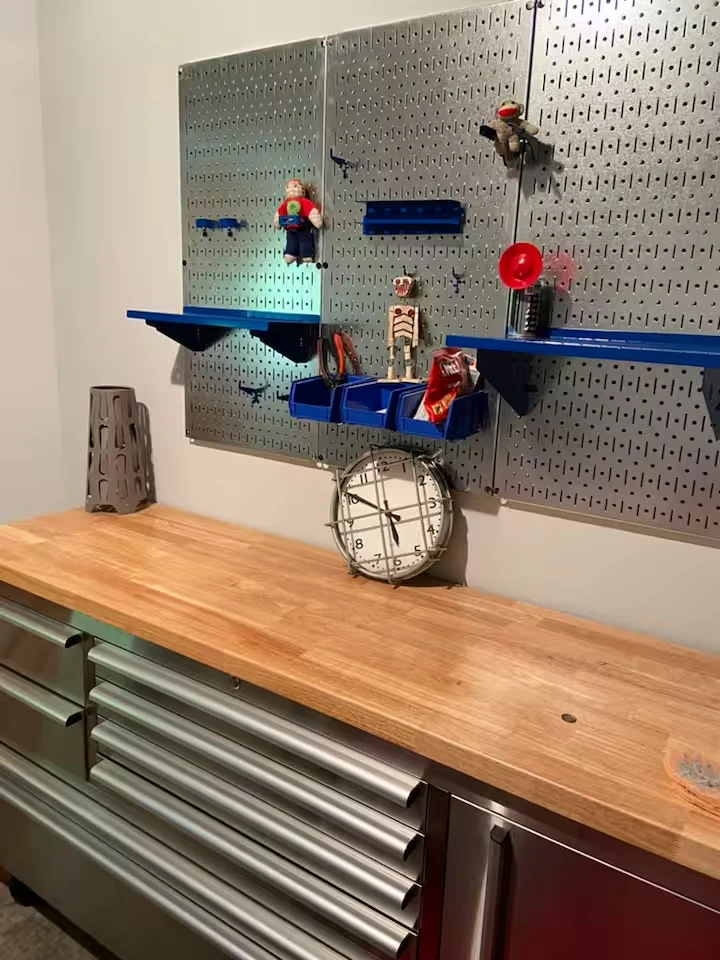 Metal tool chest with wooden countertop beneath a pegboard with blue shelves and decorative objects