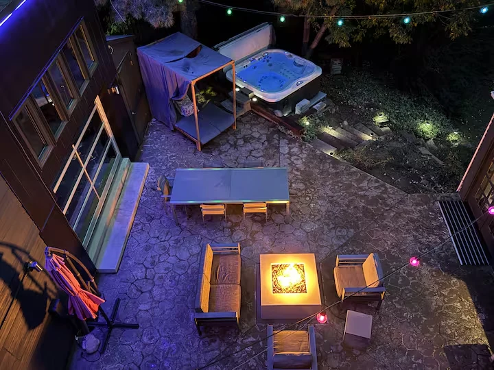 Overhead nighttime courtyard view with lit fire pit, outdoor dining table, covered lounge and hot tub