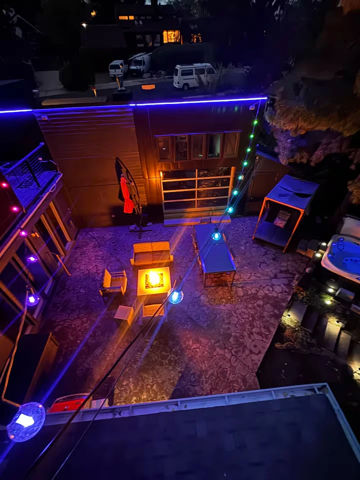 High nighttime view of the courtyard with colorful lights, central fire pit, dining table and hot tub