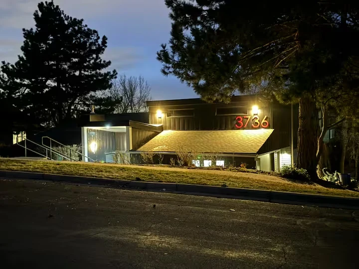 Street-facing view of the residence at dusk with warm exterior lighting and mature pine trees