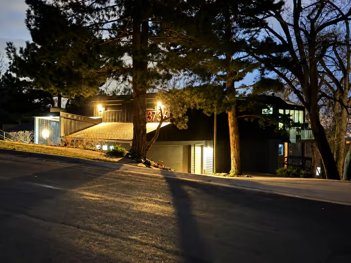 Residence viewed across a sloping neighborhood street beneath mature trees at dusk