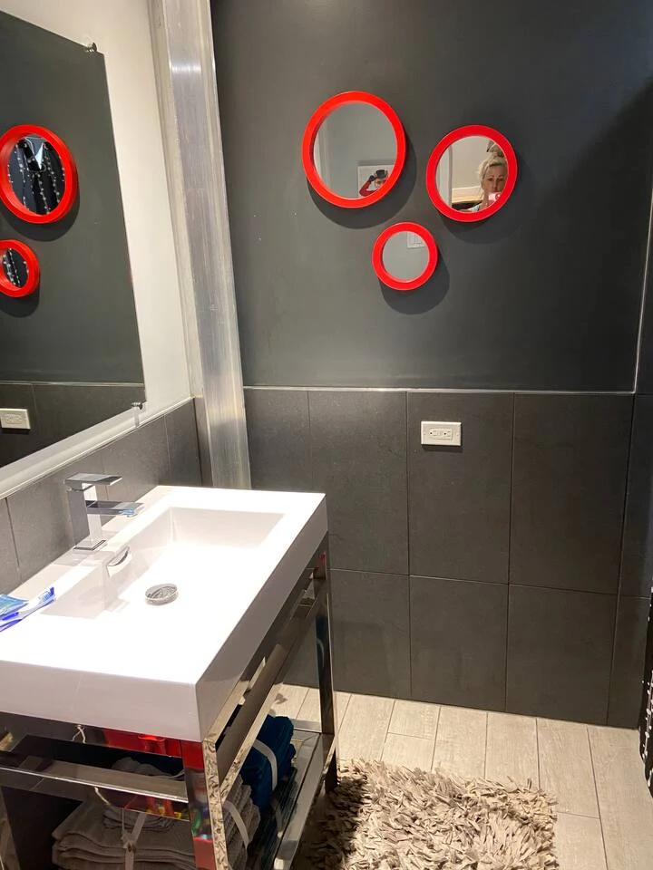 Guest bathroom vanity with rectangular white sink, chrome shelving and three red circular mirrors on a charcoal wall
