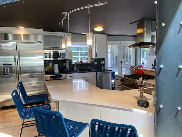 Kitchen with stainless steel refrigerator, stacked ovens, range and white breakfast counter with blue stools