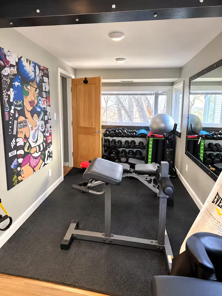 Home gym with strength-training benches, dumbbell racks, exercise ball, mirrored wall and colorful artwork
