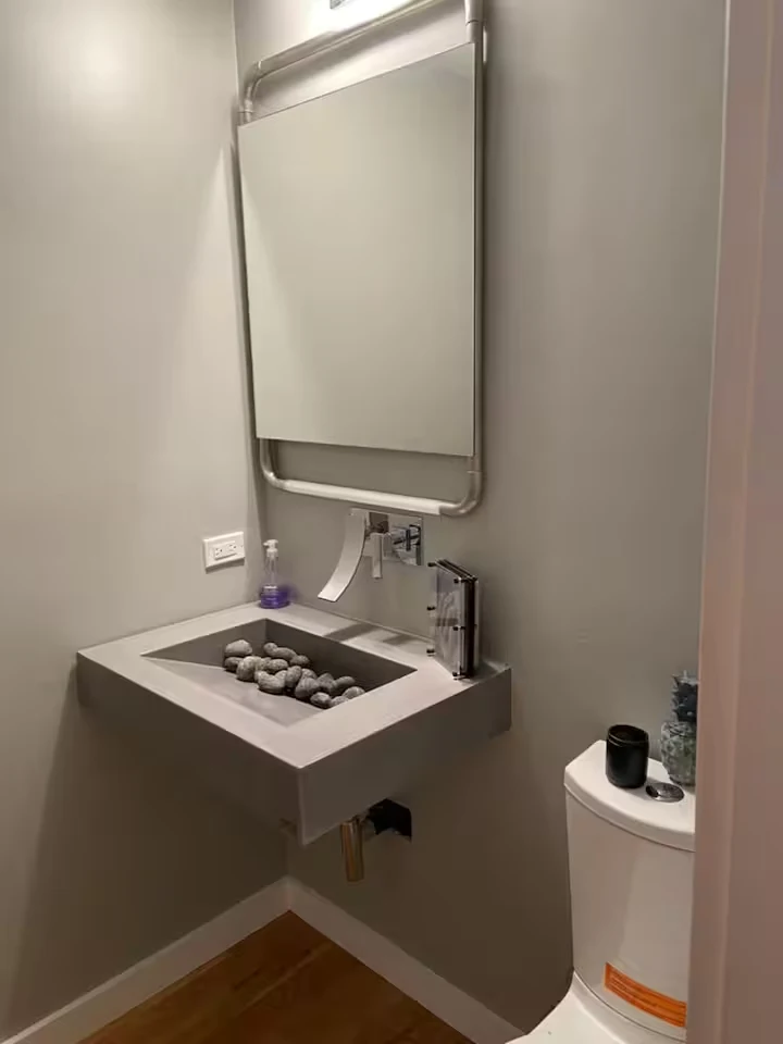 Powder room with wall-mounted concrete sink, smooth stones, metal-framed mirror and contemporary faucet