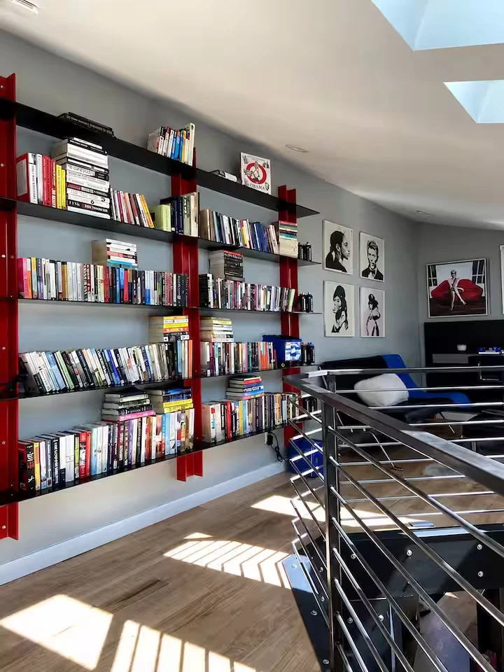 Library reading area with wall-mounted bookshelves, black and blue seating, hardwood floor and steel railing