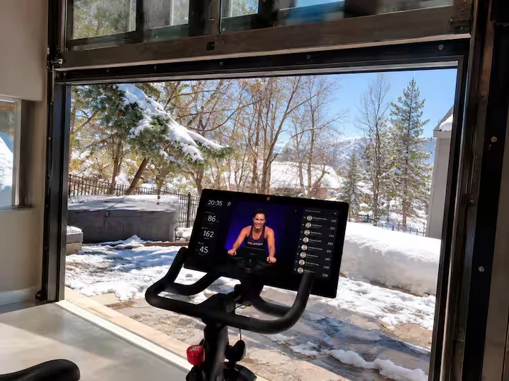 Peloton bike and display beside a large window overlooking a snow-covered backyard and trees