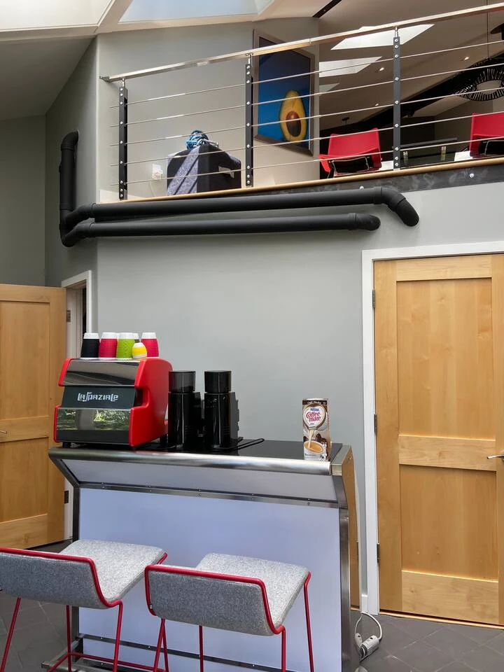 Sunroom espresso bar with red espresso machine, black grinders and two red-framed stools beneath the loft railing